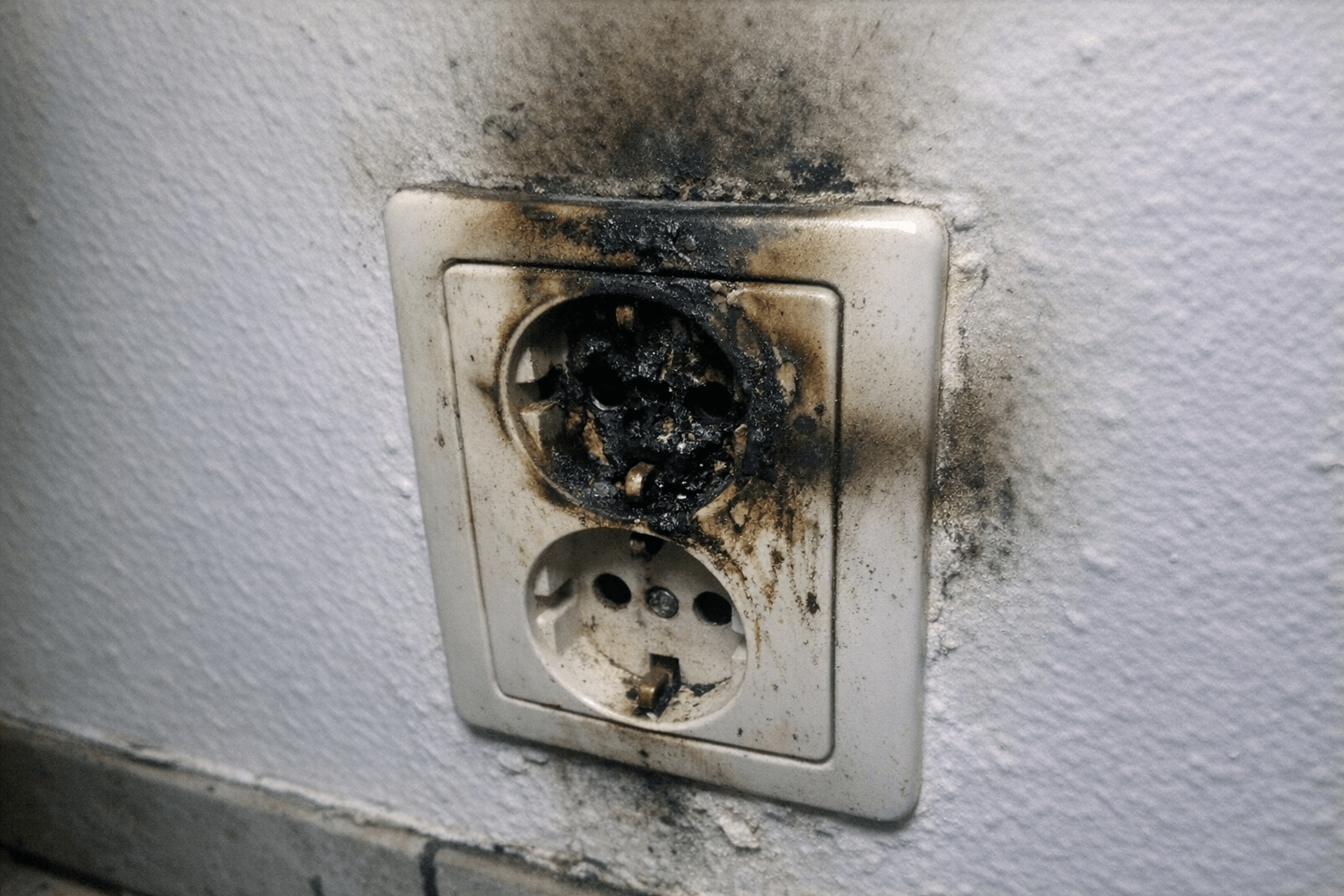 Geschwärzte Steckdose nach einem Kurzschluss im Wohnraum